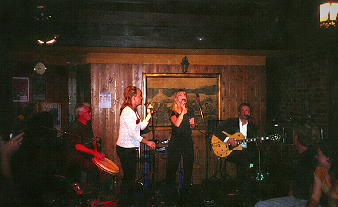 A band across a small stage with two vocalists at the microphones and a guitarist at the right.