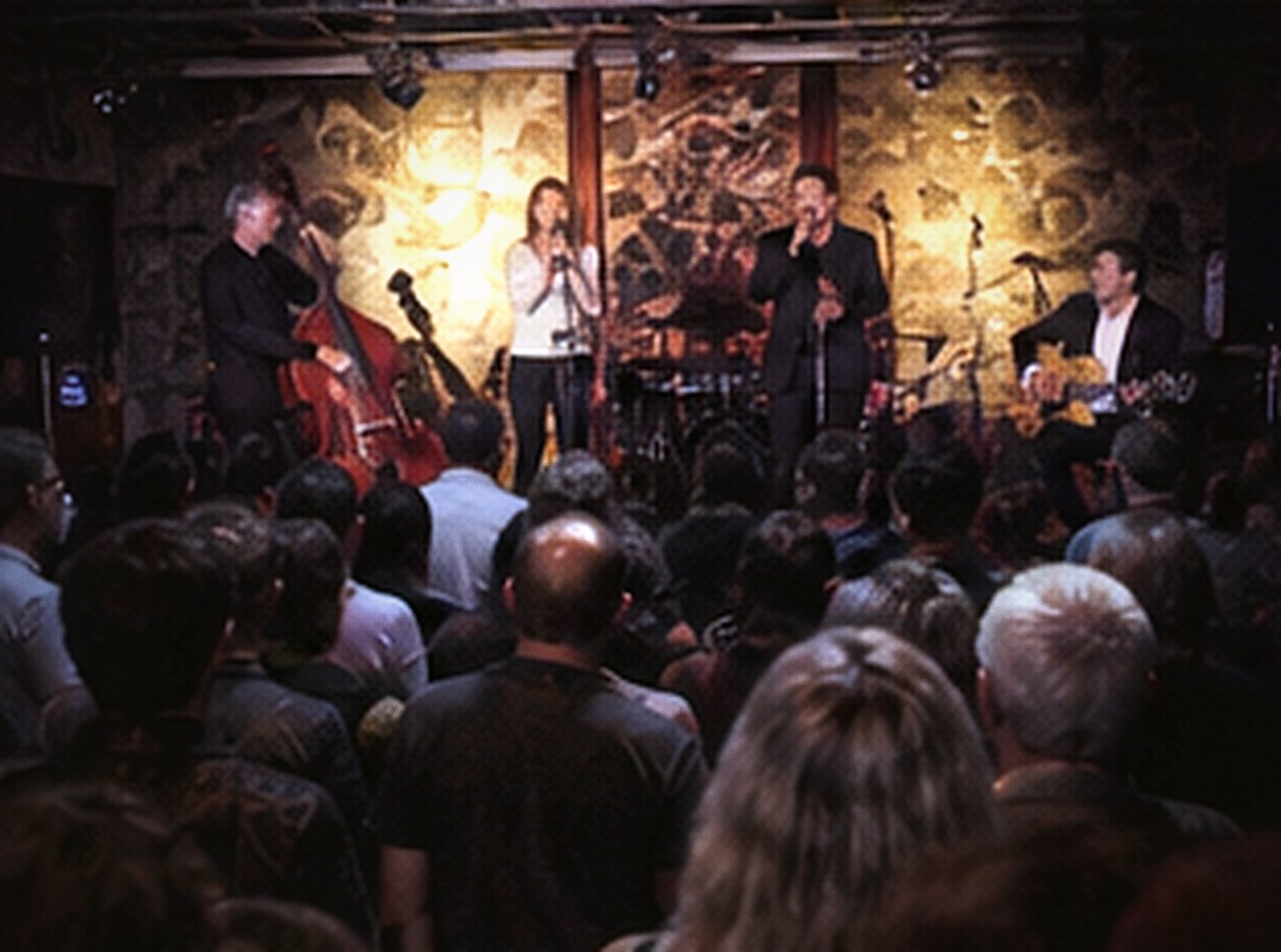 A wide stage with double bass, vocalists and full band before a large seated crowd.
