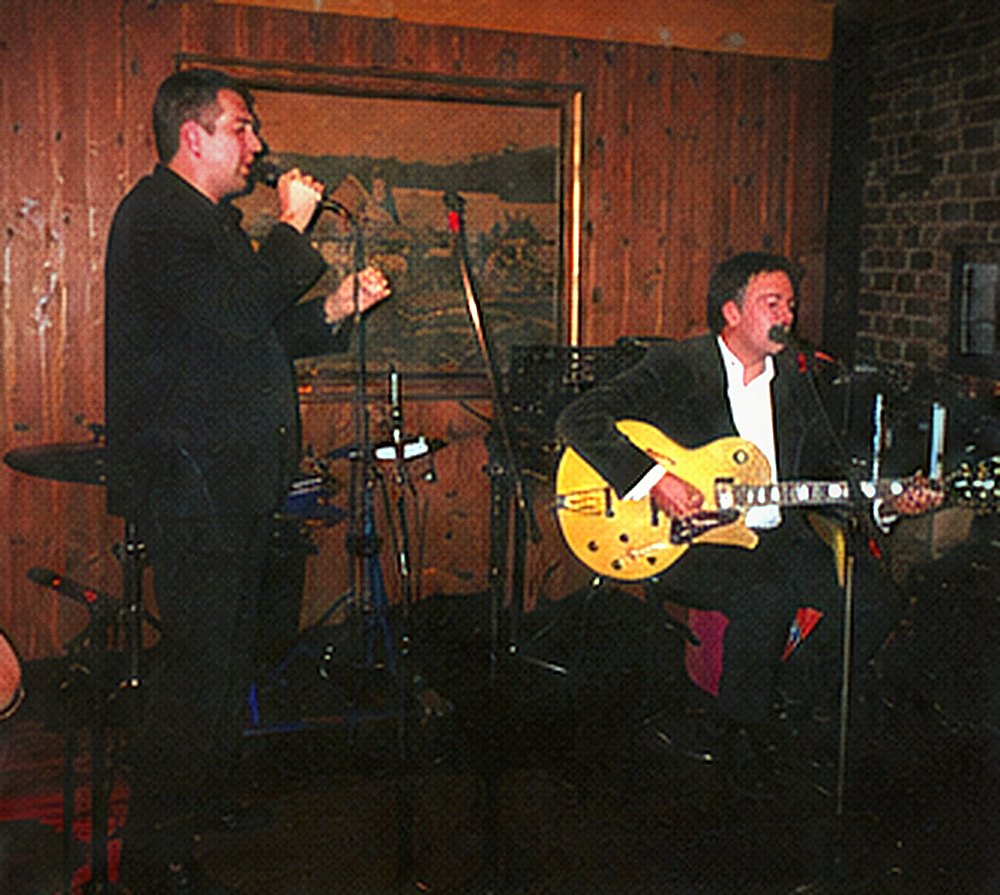 Frankie Velvet standing at a microphone stand, arms at his sides.