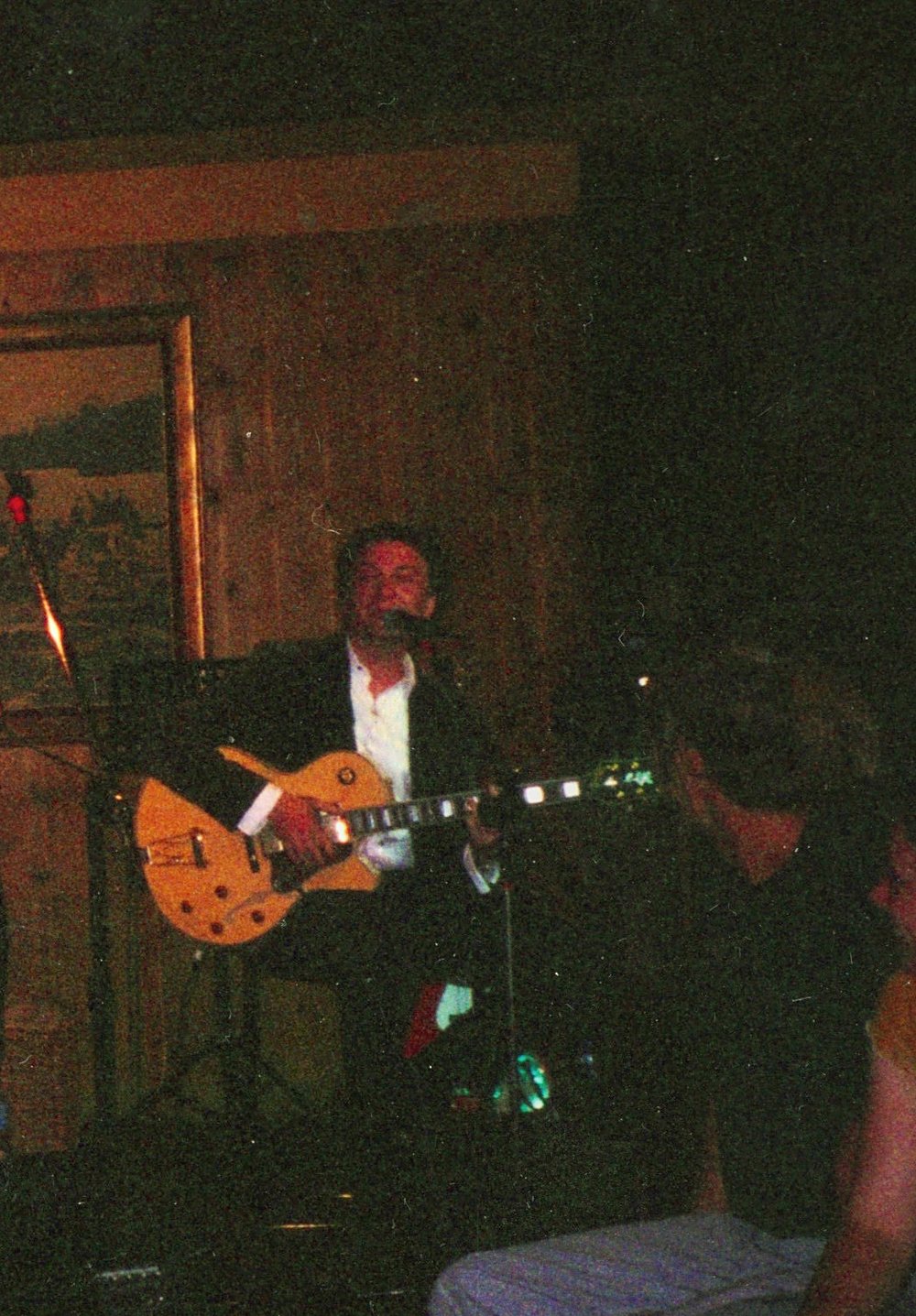 A guitarist at stage right in a dark suit, lit from above.