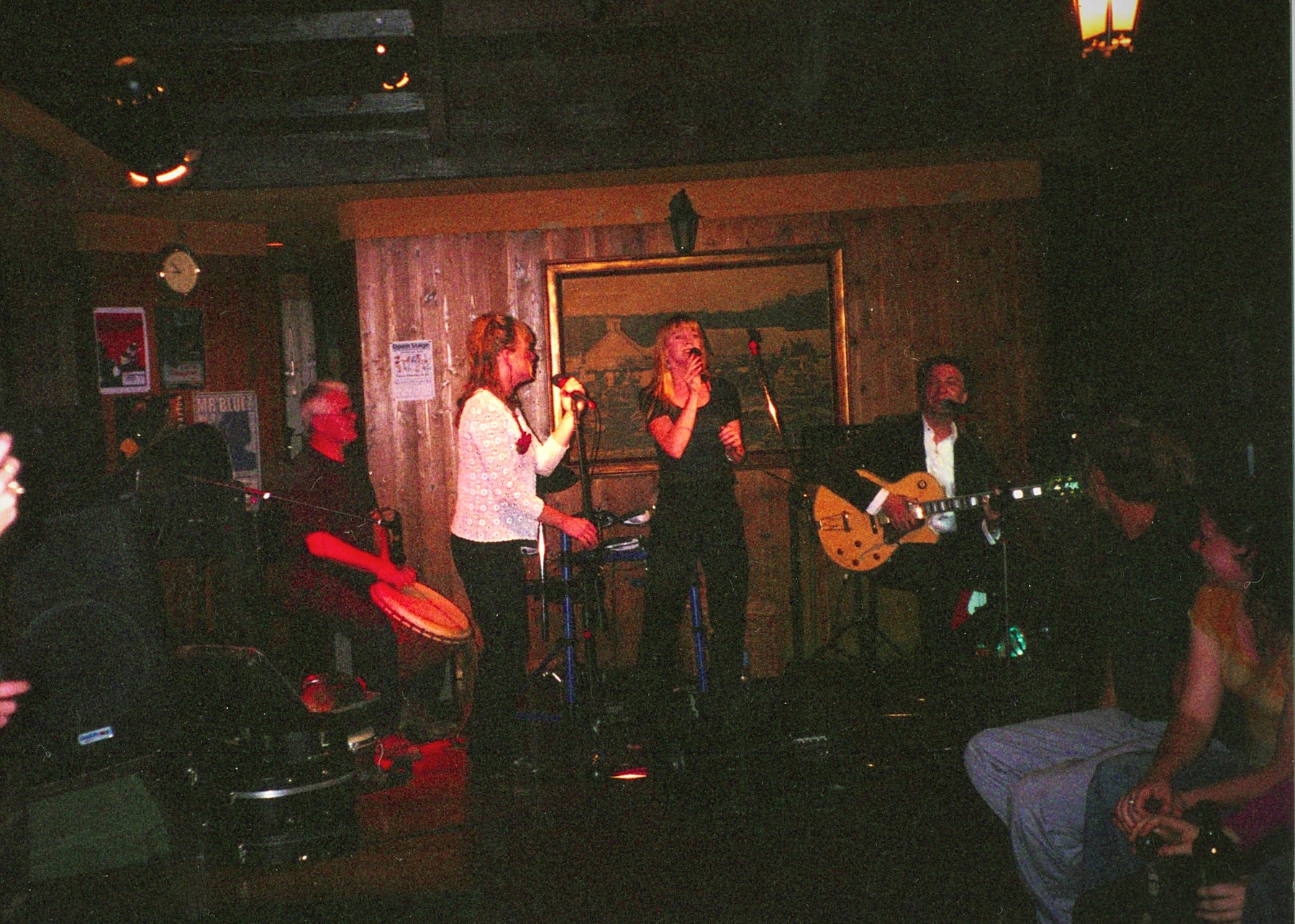 A dim panelled room, band on a low stage, patrons watching from the foreground.
